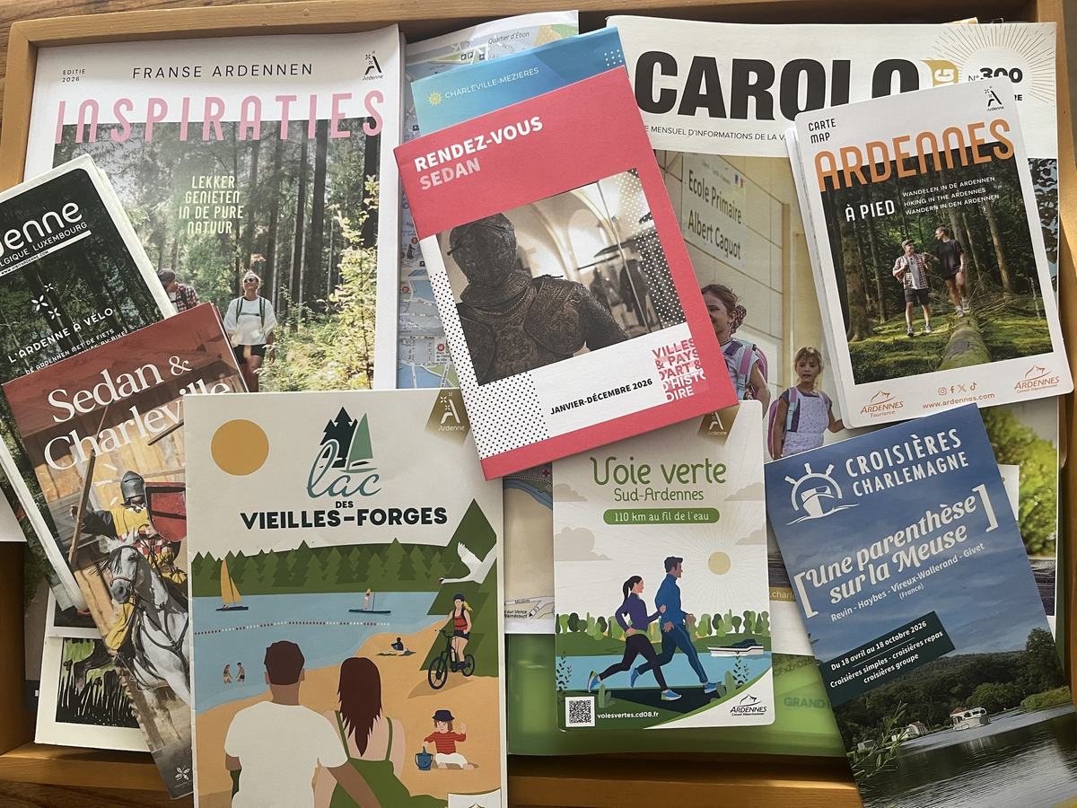 Des brochures touristiques des Ardennes sur un plateau en bois : Voie Verte, lac des Vieilles-Forges, Sedan et Charleville, croisières sur la Meuse.